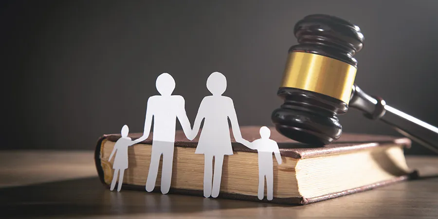 Paper cutout of a family in front of a law book and judge's gavel